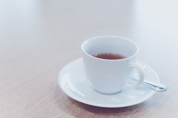 cup of hot tea and spoon on wooden table in meeting room - filter retro color tone