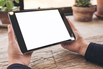 Mockup image of hands holding black tablet pc with blank white screen on vintage wooden table