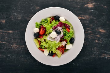 Salad with mozzarella and fresh vegetables. On a black wooden background. Top view. Copy space for your text.