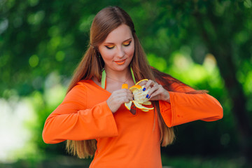 Portrait of pretty red hair woman with juicy delicious orange at summer green park.