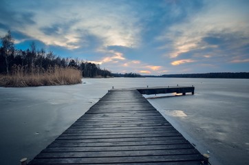 Avond winterlandschap. Houten pier over een prachtig bevroren meer.