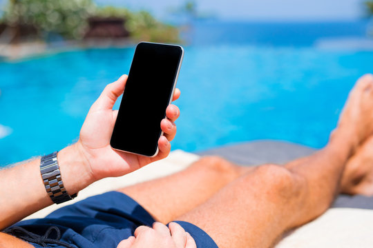 Man holding phone on vacation by the pool
