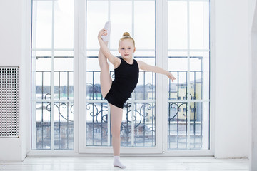 Fototapeta na wymiar Little Child Girl gymnast doing stretching in a bright room on a happy and cute window background
