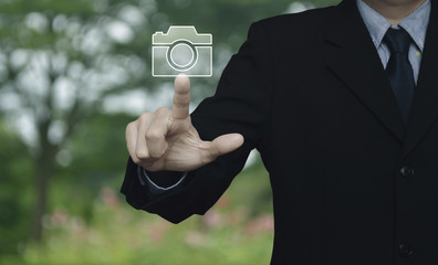 Businessman pressing camera flat icon over blur flower and tree in park, Business camera service concept