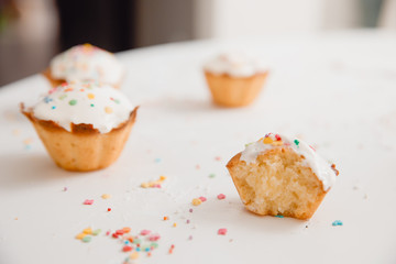 close-up of a bitten cupcake, in the background cupcakes with white cream and colored caramel for Easter.