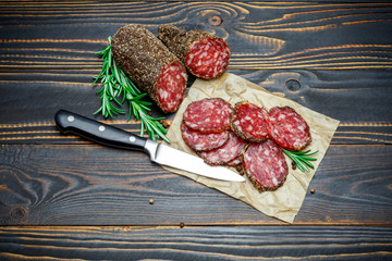 Dried organic salami sausage covered with pepper on wooden background