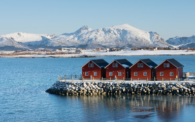 typical norwegian red houses on stone pier with mountains in background - obrazy, fototapety, plakaty
