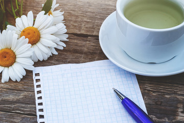 Cup of tea with flowers and page on table close up