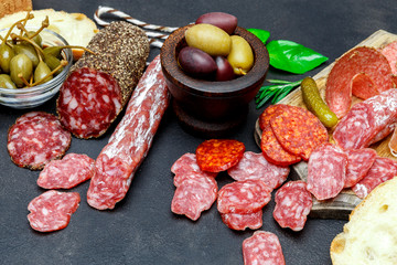 Cutting board with salami, bread, olives and capers