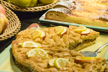 Closeup of an apple pie on a tray. Apple pie with apple and lemon slices, yellow and red apples details in background.