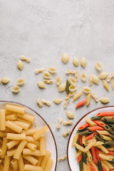 top view of various raw pasta in bowls on messy concrete tabletop