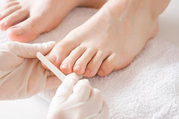 Zelfklevend Fotobehang Pedicurist's hands in protective rubber gloves filing toenails with nail file. Cares about man's feet. Specialist with client in beauty salon. Professional beauty service. Pedicure, manicure concept. © fotoduets