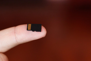 Micro sd card in human fingers on brown background with copy space