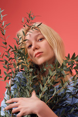 attractive young woman with bunch of boxwood branches isolated on red