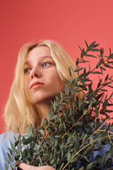 Naklejka premium beautiful young woman with bunch of boxwood branches isolated on red