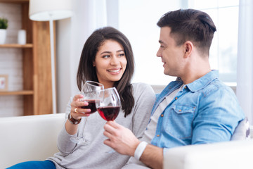 Red wine. Inspired optimistic couple clinking glasses with wine while smiling