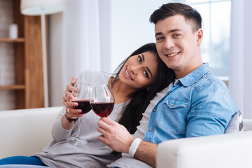 Wine for mood. Vigorous exuberant couple holding glasses with wine while looking at camera