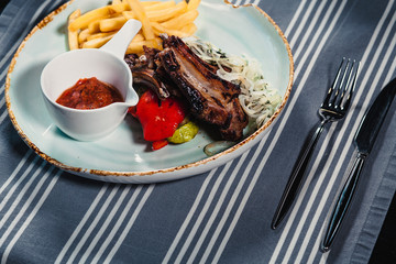 Plate with rack of lamb, grilled vegetables, bow, sauce and french fries. Clouse up