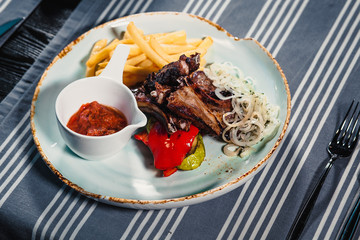 Plate with rack of lamb, grilled vegetables, bow, sauce and french fries. Clouse up. On the background of a table with a tablecloth