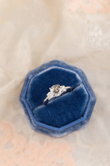 Fototapeta na wymiar White golden wedding ring with diamonds in blue vintage velvet ring box on pink lace background
