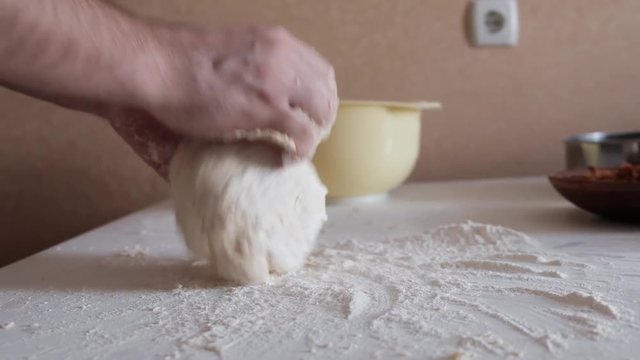 Male hands kneading dough in flour on a table. Slow motion.
