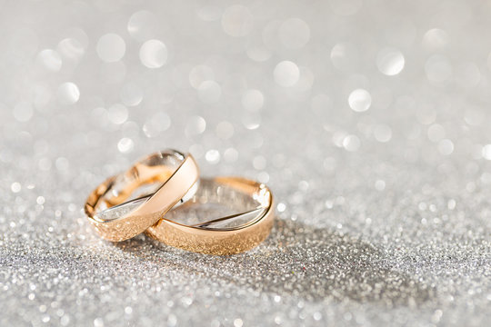 Silver sparkling glitter bokeh background with golden wedding rings