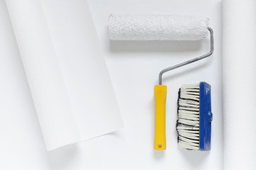 paint roller and a brush on white wallpaper roll