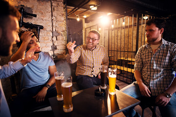 Cheerful smiling man showing wedding ring on his hand to confused friends while sitting in the pub.