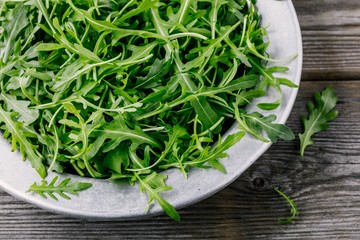 Fresh green arugula salad leaves in a bowl on a wooden background. Top view
