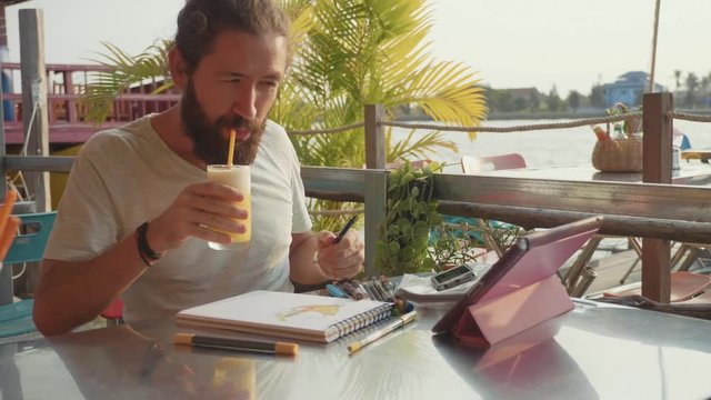 Male designer draw sketches in open air riverside cafe in slow motion.