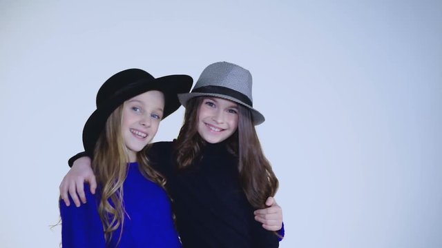Two young girls in hat dancing and posing at camera on background
