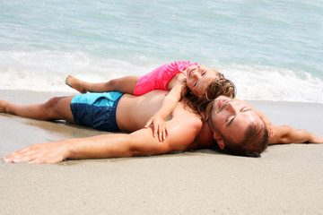 Father and daughter lying together on the beach.