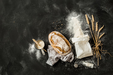Bread, flour bag, wheat and measuring cup on black