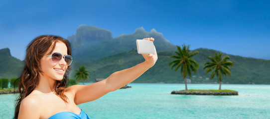 travel, tourism, summer holidays and vacation concept - happy young woman taking selfie by smartphone at touristic resort over bora bora island beach background