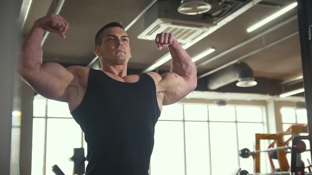 Sportive man bodybuilder posing and shows muscles near mirror in the gym