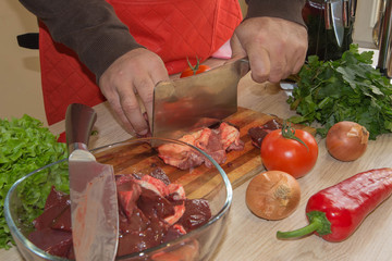 Cook cutting meat on a board and fresh raw vegetables on a table. Food concept