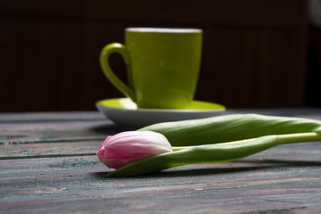 A cup of coffee and pink tulips flowers on wooden background.