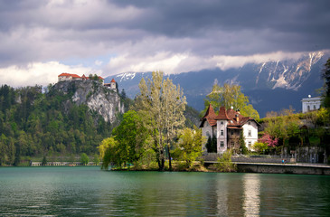 Fototapeta na wymiar Scenic view of Lake Bled with castle, villas and mountains covered by clouds on background at springtime, Slovenia