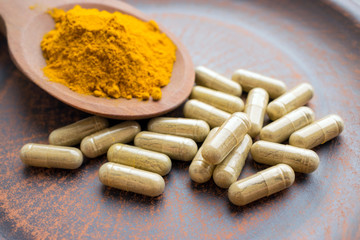 Natural herb food supplement turmeric veggie capsules and spoon with orange curcumin powder on clay...