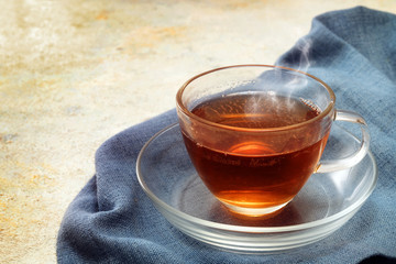 freshly brewed black tea in a glass cup, steaming hot drink on a blue napkin, copy space