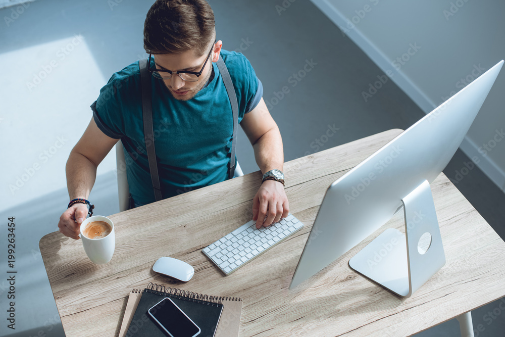 Aufkleber overhead view of young freelancer drinking coffee while working with desktop computer