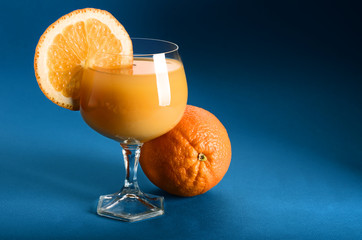 Orange juice in a glass with whole orange on side on blue background with place for text