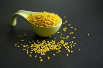 Croup of bulgur placer, pile on a black background lined in a spoon, a bowl. The product is rich in protein, healthy food, vegetarianism. View from above. Side view. Close up