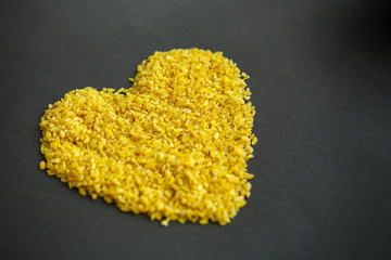 Croup of bulgur placer, pile on a black background lined in the form of a symbol of the heart,...