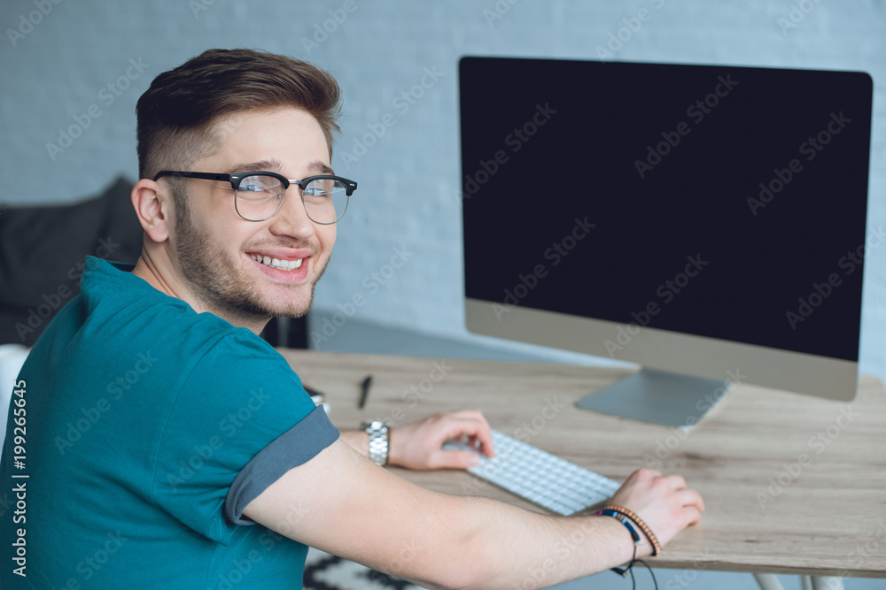 Poster smiling designer working by table with desktop computer