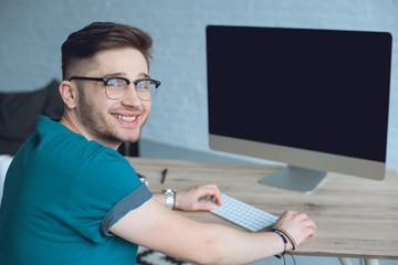 Smiling designer working by table with desktop computer
