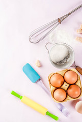Ingredients and utensils for cooking baking egg, flour, sugar, whisk, rolling pin, on light pink background, top view copy space