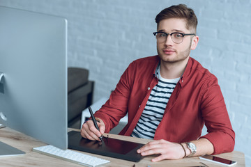 Man freelancer at work by table with computer and graphic tablet