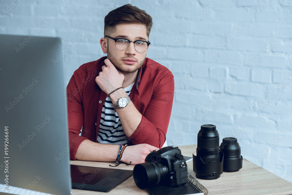 Aufkleber young bearded man by working table with camera and computer