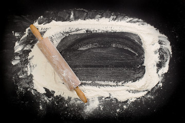 background with flour sprinkled on a black table with a rolling pin on the side